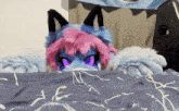 a stuffed animal with purple eyes and pink hair is laying on a bed
