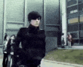 a man in a black jacket is walking in front of a building