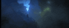 a person is standing in a dark cave with a blue light coming out of the ceiling .