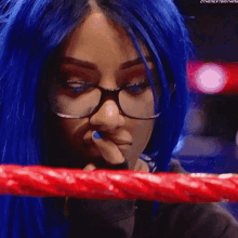 a woman with blue hair and glasses is standing in a red ring