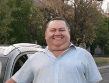 a man in a blue shirt is smiling in front of a car .