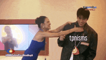 a woman in a blue dress is hugging a man in a black jacket with tpnisms written on it