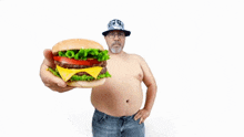 a shirtless man is holding up a hamburger with lettuce and tomatoes
