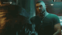 a man in a green shirt is talking to another man in a dark room with # xboxe3 written on the bottom