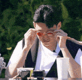 a man wearing sunglasses sits at a table with a cup of coffee in front of him
