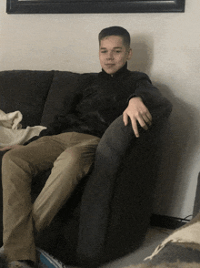 a young man sits on a couch with his hand on the armrest