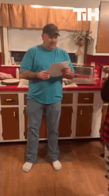 a man in a blue shirt is standing in a kitchen holding a piece of paper with the letters th above him