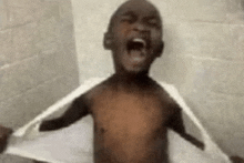 a shirtless child is taking a shower with a towel over his shoulders .