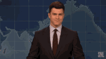 a man in a suit and tie stands in front of a snl sign