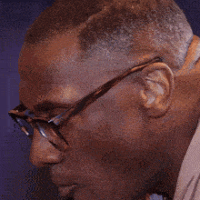 a man wearing glasses sits on a couch eating a meal