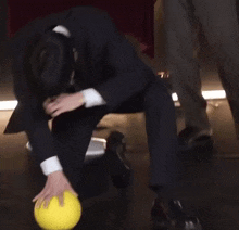 a man in a suit is kneeling down on the floor holding a yellow ball