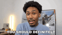 a man in a blue sweater says you should definitely in front of a microphone