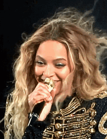 a woman singing into a microphone wearing a gold and black jacket