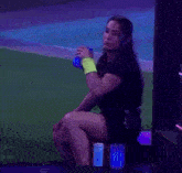a woman in a black dress is sitting on a stool holding a blue cup .