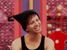 a man wearing a black tank top and a black beanie is smiling