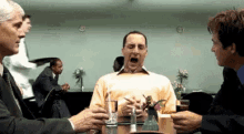 a group of men are sitting at a table with a man yawning .