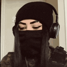 a woman wearing a beanie and headphones is covering her face with a mask .