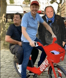 two men are riding a red bicycle that says jump on it