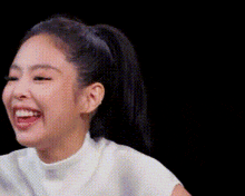 a close up of a woman 's face with a ponytail laughing on a black background .