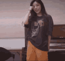 a woman is standing in front of a piano wearing a black shirt and orange pants .