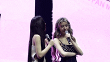 two women are standing next to each other on a stage with microphones .
