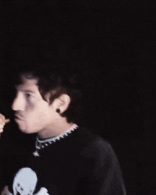 a man wearing a black shirt with a skull and crossbones on it is eating a snack