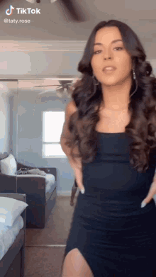 a woman in a black dress is dancing in a room with a ceiling fan behind her
