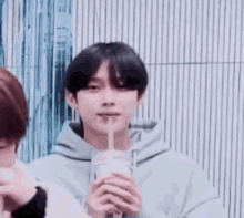 a young man in a blue hoodie is drinking from a cup with a straw .