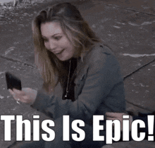 a woman sitting next to a man looking at her phone with the words " this is epic " below her