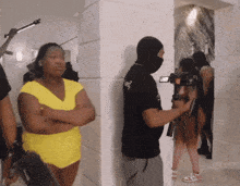 a man wearing a mask holds a camera while a woman in a yellow top looks on