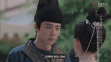 a man and a woman are looking at each other and the man is saying " here you are "
