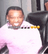 a man in a pink shirt is sitting in a chair and says " say dada " in the corner