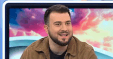 a man with a beard is smiling while sitting in front of a television screen .