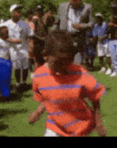 a boy in an orange and blue striped shirt is running in a field .