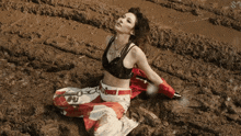 a woman in a crop top sits in the mud with the letter s on the bottom right