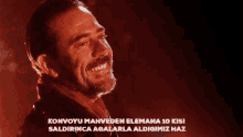 a man with a beard is smiling in front of a red background with the words konvoyu mahveden elemana 10 kisi
