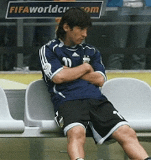a soccer player sits on a bench with his arms crossed in front of a fifa world cup sign