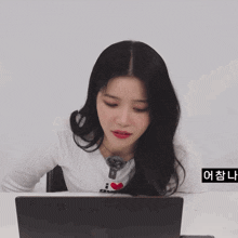 a woman wearing a shirt that says i love gu is sitting in front of a laptop