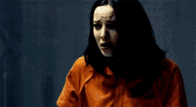 a woman in an orange prison uniform is standing in front of a glass wall .