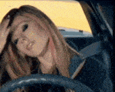 a woman is sitting in a car with her hand on her head .