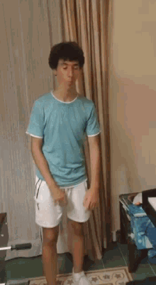 a young man in a blue shirt and white shorts is standing in front of a curtain .