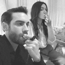 a black and white photo of a man smoking a cigarette next to a woman
