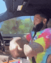 a man wearing a tie dye shirt is sitting in a car