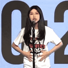 a woman stands in front of a microphone wearing a shirt that says just sweet ost