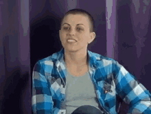 a woman with a shaved head is wearing a blue and white plaid shirt and smiling .