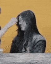 a woman with long hair is sitting at a table while another woman touches her hair .