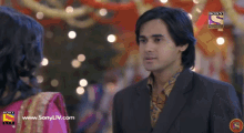 a man in a suit stands in front of a woman in a pink dress and a sony tv logo