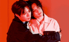 two men are hugging each other in front of a red background