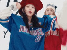 a woman wearing a blue new york jersey is standing next to another woman wearing a red hat