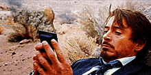 a man in a suit and tie is laying on the ground looking at his cell phone